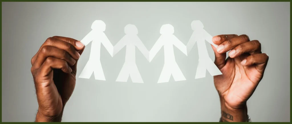 Hands holding up a chain of paper people representing working together against systemic racism.